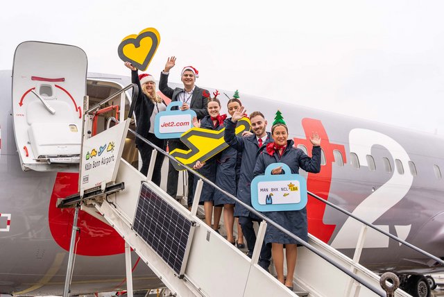 Mehrere Personen stehen auf einer Flugzeugtreppe, schauen in die Kamera und halten Schilder hoch.
