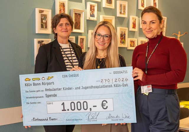 Zwei Flughafen-Mitarbeiterinnen übergeben einen symbolischen Spendenscheck über 1.000 Euro an den Hospitzverein.