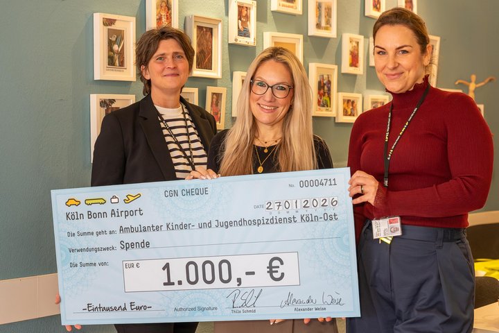 Zwei Flughafen-Mitarbeiterinnen übergeben einen symbolischen Spendenscheck über 1.000 Euro an den Hospitzverein.