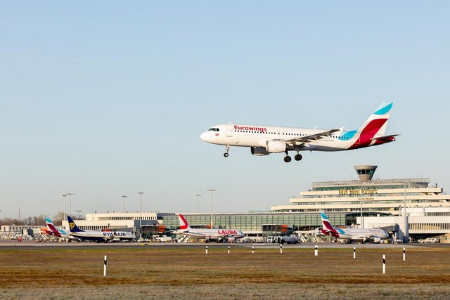 Ein Eurowings Flugzeug im Landeanflug, im Hintergrund das Terminal 1 des Köln Bonn Airport