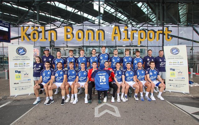 Die Handball-Mannschaft des TV Jahn Köln-Wahn steht in Flughafen Trikots vor dem Terminal 2.
